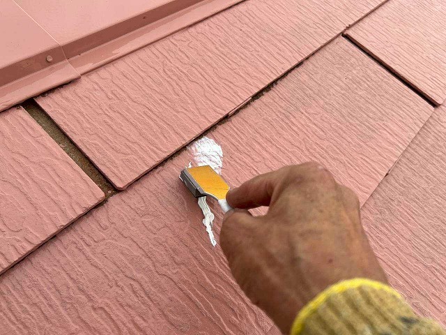 屋根のひび割れにシーリングを充填しヘラで整える作業